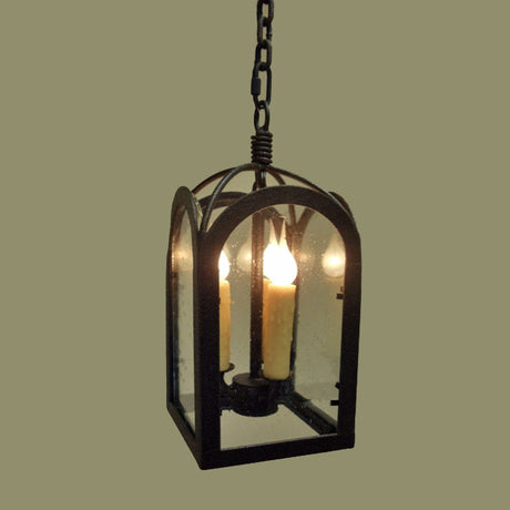 A decorative pendant light featuring a black wrought iron frame with arched details and transparent panels. It includes three candle-like bulbs that create a warm, inviting glow, suspended by a sturdy chain.