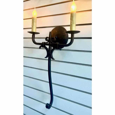 A black wrought iron wall sconce featuring two candle-like lights above a decorative circular accent. The elegant design, with scroll details, adds warmth and ambiance to any space.