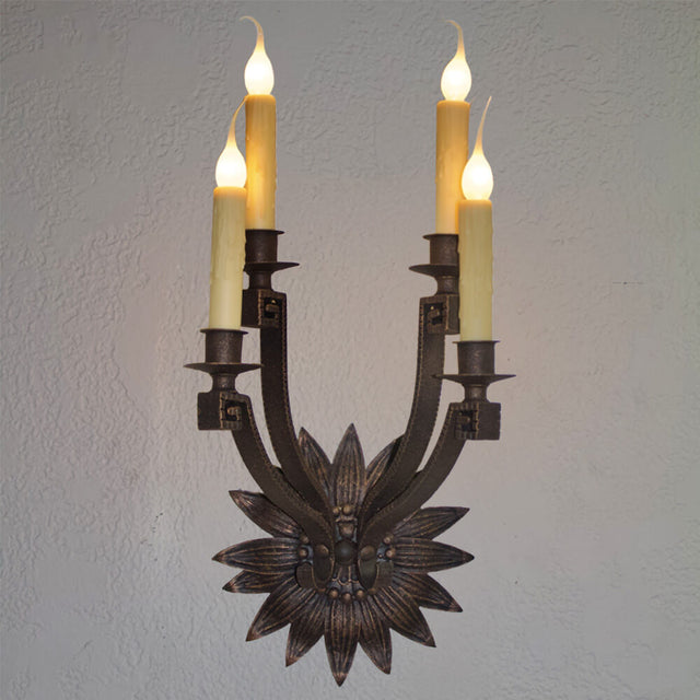 Spanish-style wrought iron sconce featuring a floral motif at the base and four candle-style lights with warm, glowing flames. The rustic design evokes classic Mediterranean elegance, ideal for adding character to traditional or vintage interiors.