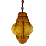 A beautifully crafted pendant featuring a twisted wrought iron frame showcasing a rounded, amber glass design. The warm glow emanates from the ornate glass, creating an inviting atmosphere. This unique fixture seamlessly blends artistry with function, ideal for enhancing any space with its distinctive charm.