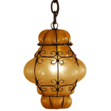 An intricately designed pendant light featuring a curvy, amber glass shade wrapped in elegant wrought iron detailing, perfect for adding warmth and character to any space.