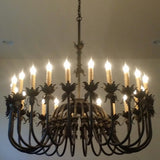 A beautifully crafted wrought iron chandelier featuring a circular design with ornate accents and multiple candle-style lights, illuminating a warm glow. The intricate detailing adds elegance, perfect for enhancing any room's ambiance.