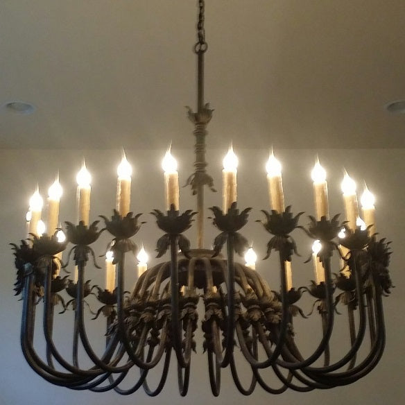 A beautifully crafted wrought iron chandelier featuring a circular design with ornate accents and multiple candle-style lights, illuminating a warm glow. The intricate detailing adds elegance, perfect for enhancing any room's ambiance.