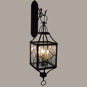 A wrought iron wall sconce featuring a geometric glass design with four candle-style bulbs inside. The elegant framework adds a decorative touch, perfect for enhancing indoor or outdoor spaces.