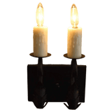 A decorative wall sconce featuring two candle-like bulbs on a black wrought iron base. The design includes intricate details and a rustic finish, ideal for adding warmth and charm to any space.