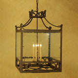 A square hanging light fixture with intricate wrought iron detailing and a glass enclosure. Inside, four candle-like bulbs provide illumination, enhancing the elegant design. Perfect for adding a touch of classic charm to any space.