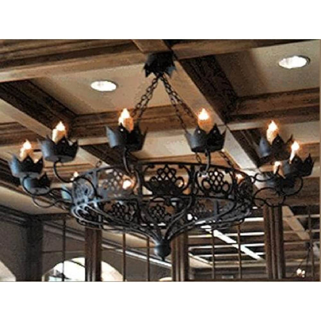 A decorative wrought iron chandelier featuring intricate scrolling designs and candle-like fixtures, suspended from a ceiling with wooden beams. The piece showcases a blend of elegance and artistry, illuminating the space with a warm glow.