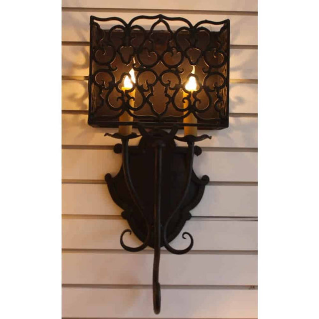 A decorative wrought iron sconce featuring an ornate design with a patterned metal shade. It holds two candle-like bulbs, casting a warm glow against a neutral background. Ideal for adding elegance to any space.