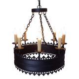 A circular wrought iron chandelier featuring six candle-like lights, each atop a slender, decorative holder. The design includes intricate detailing along the edges and is suspended by a chain, creating an elegant and rustic ambiance.