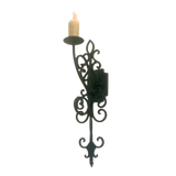 A decorative wrought iron wall sconce featuring intricate scrolling designs, holding a single candle. The elegant craftsmanship enhances any space with a warm, inviting glow.