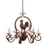 A decorative wrought iron chandelier featuring a central rooster motif surrounded by elegant scrollwork. It has six candle-style lights, each warmly illuminated, showcasing intricate craftsmanship and rustic charm, perfect for enhancing any space's character.