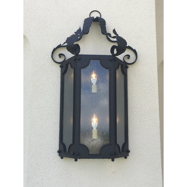 A decorative wall sconce featuring a wrought iron frame with elegant scrollwork and leaf motifs. The design showcases three candle-like lights within clear glass panels, providing a warm ambiance. Perfect for adding charm to entryways or outdoor spaces.