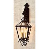 A decorative wall sconce featuring intricate wrought iron detailing and a glass enclosure, housing three glowing candles for a warm ambiance.