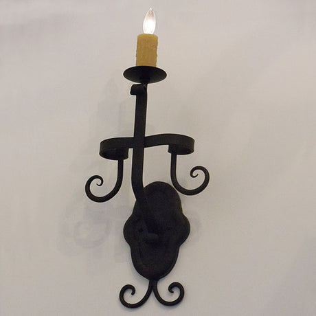 A beautifully crafted wrought iron wall sconce featuring intricate scrollwork and a single candle holder. The design showcases a textured base and graceful curves, ideal for adding warm ambiance to any interior space.