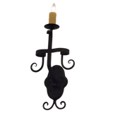 A decorative wall sconce featuring elegant curves and a candle holder design. The piece is crafted from wrought iron, showcasing a rustic charm perfect for adding warmth and ambiance to any space.