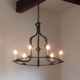 A decorative wrought iron chandelier featuring six glowing candle-like bulbs. The curved lines and intricate detailing create a classic and warm ambiance, making it an elegant centerpiece for dining or living spaces. The fixture is suspended by a chain, enhancing its timeless charm.