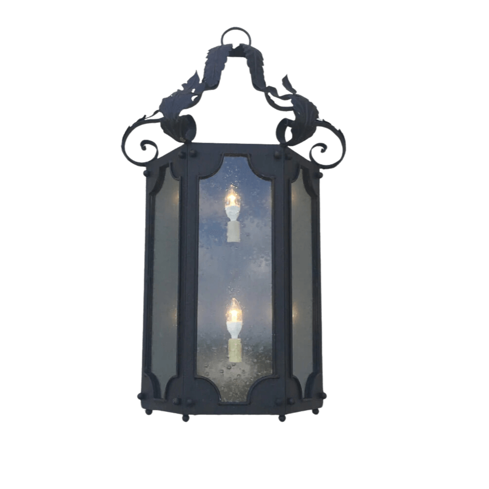 A beautifully crafted wrought iron sconce featuring a decorative top and intricate scrollwork, showcased with three light bulbs behind textured glass panels, enhancing elegance and warmth.