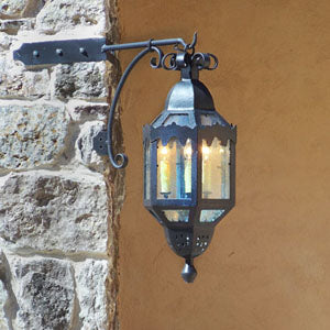 A decorative wrought iron sconce featuring a lantern-style design, accented with intricate cutouts and a curved arm, illuminating with multiple bulbs.