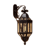 A decorative wrought iron wall sconce featuring an ornate design with glass panels, showcasing its warm glow. Ideal for adding traditional charm to any space.