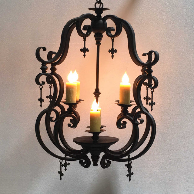 A beautifully designed wrought iron chandelier featuring intricate curls and elegant detailing. It holds three candles, each illuminating softly with flickering flames. The piece combines ornate aesthetics with a warm ambiance, perfect for enhancing any space.