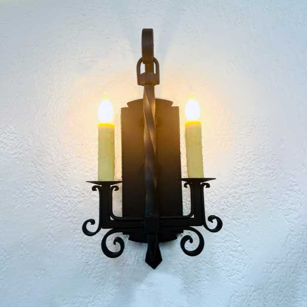 Elegant wrought iron sconce featuring two twisted candles set against an ornate backplate, radiating warm light. Ideal for enhancing rustic decor.