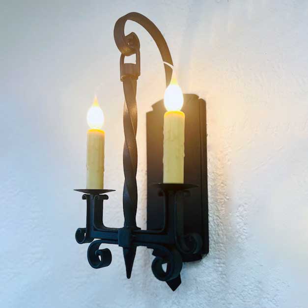 Elegant wrought iron wall sconce featuring two candle-style lights with decorative twisted arms, showcasing intricate detailing and a classic design.