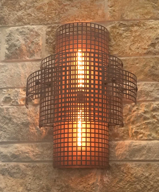 A stylish wrought iron sconce featuring a grid design, casting warm light against a textured stone wall, enhancing a rustic ambiance.