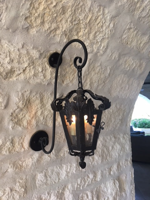 Intricately designed wrought iron sconce featuring decorative scrollwork and a lantern-style shade that beautifully illuminates the surrounding space.