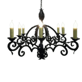 A decorative wrought iron chandelier featuring elegant scrollwork and six candle-like bulbs. The fixture has a dark finish and intricate detailing, perfect for adding warmth and style to any space.