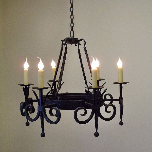 A beautifully crafted wrought iron chandelier featuring an elegant design with intricate scrollwork. It has six candle-style lights with soft, flickering flames, suspended from a sturdy chain. The overall finish adds a rustic yet refined touch, perfect for enhancing the ambiance of any room.