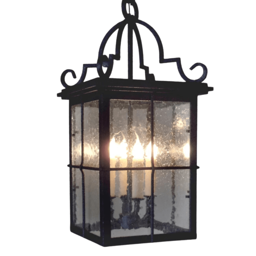 A decorative pendant light featuring a black wrought iron frame with intricate detailing. The clear panels showcase warm candle-style bulbs inside, providing an elegant glow. Designed to enhance both indoor and outdoor spaces.