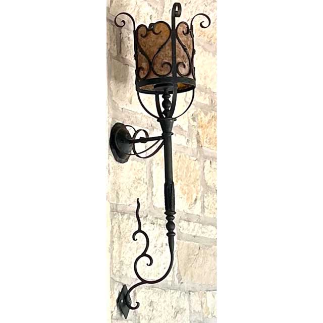 A decorative wall sconce featuring intricate wrought iron craftsmanship. The fixture has a curved design with a cylindrical shade, showcasing elegant scrollwork. Ideal for enhancing the ambiance of any space with warm and inviting light.