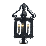 A detailed wrought iron sconce featuring intricate designs and three illuminated candle-style bulbs. The piece showcases elegant curves and ornate embellishments, perfect for enhancing any space with a warm ambiance.