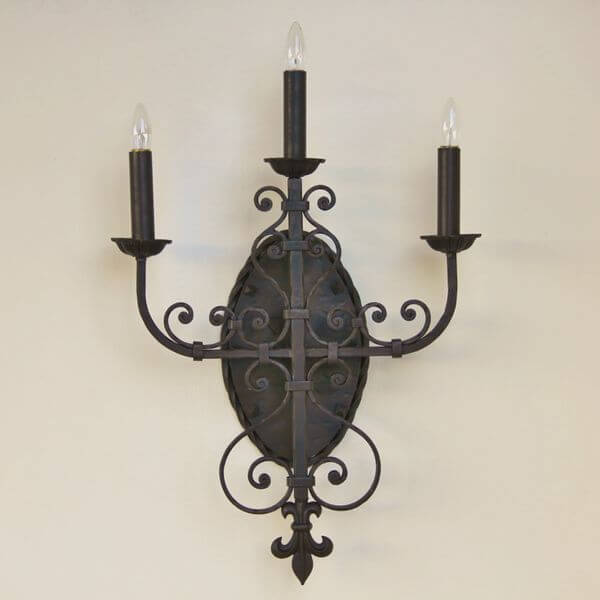 A decorative wall sconce featuring intricate wrought iron designs, three candle-like bulbs, and a central oval plate, perfect for adding elegance to any space.