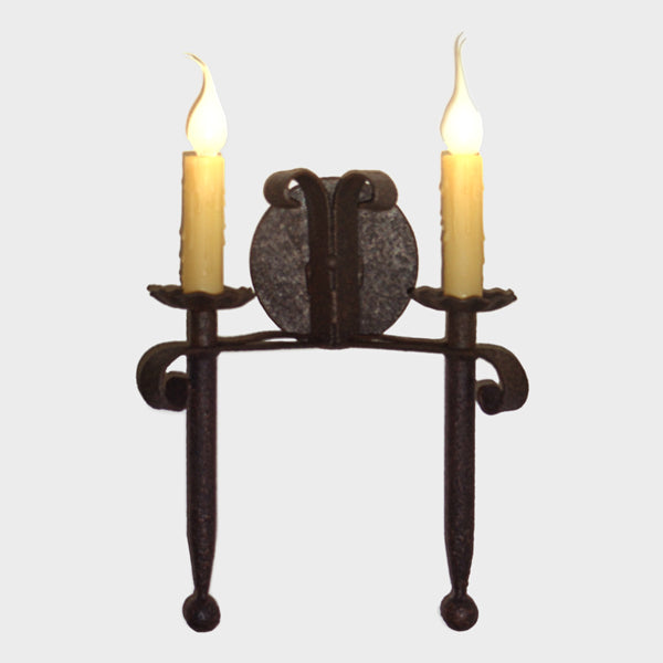 A beautifully crafted wall sconce featuring two flickering candle lights atop elegant curved supports and a decorative backplate. The fixture exudes rustic charm, perfect for enhancing cozy interiors.