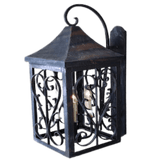 A decorative wall-mounted sconce featuring intricate wrought iron scrollwork. Its peaked top adds architectural interest, and it holds candle-like bulbs for warm illumination.