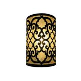 A cylindrical wall sconce featuring intricate, swirling wrought iron patterns. The design contrasts with the warm glow of light emanating from within, creating a cozy and elegant atmosphere.