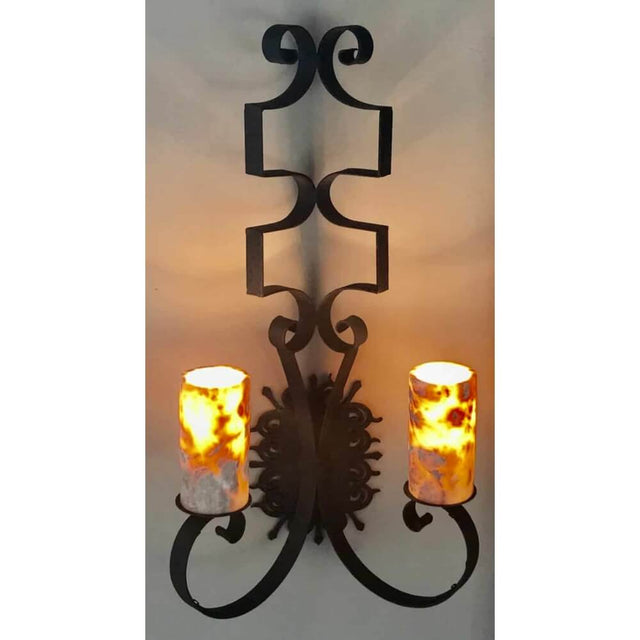 A decorative wrought iron wall sconce featuring elegant scrollwork and two glowing candle-like fixtures. The intricate design adds a warm, inviting touch to any space.