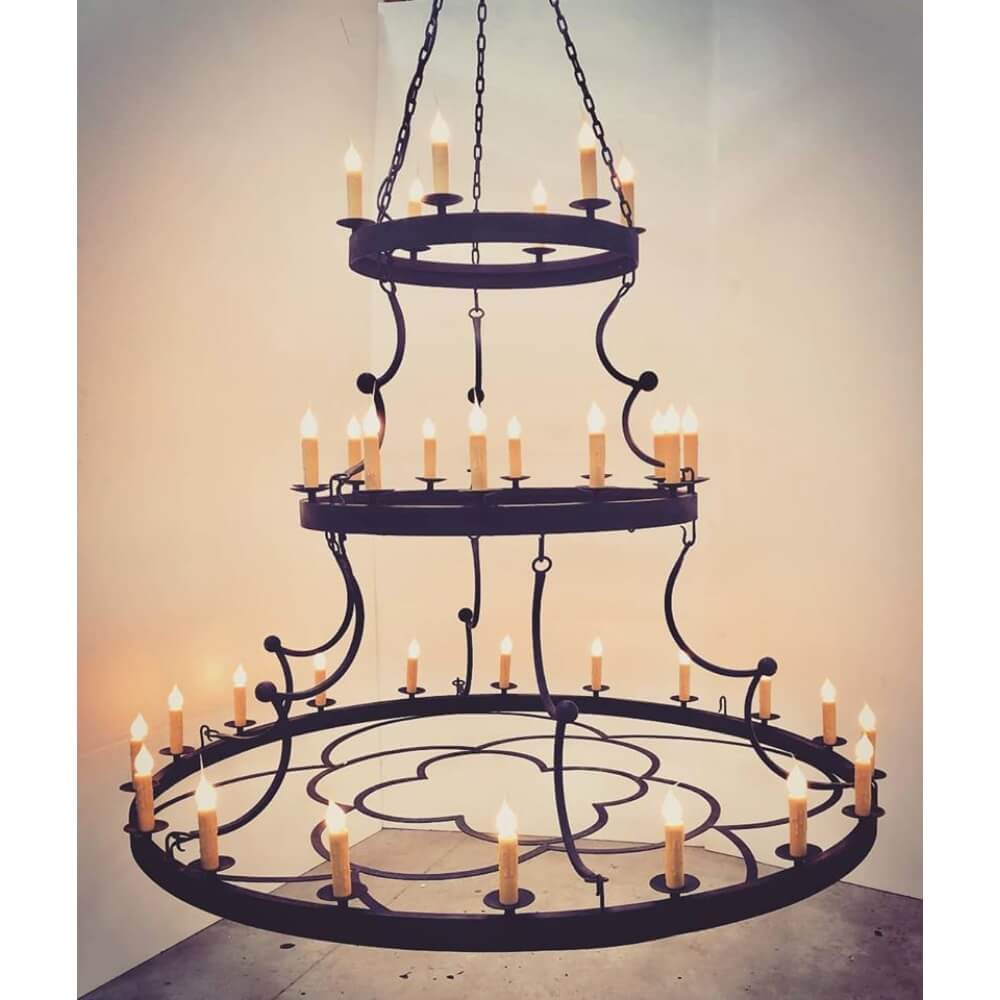 A large, multi-tiered chandelier featuring a dark wrought iron frame and decorative swirls. It holds numerous candle-like lights, exuding warmth and elegance, perfect for creating a cozy atmosphere in various settings.