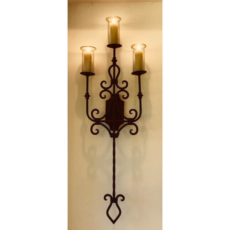 A three-arm wall sconce featuring elegant wrought iron design, accented by glass candle holders. The fixture adds a touch of warmth and sophistication to any space.