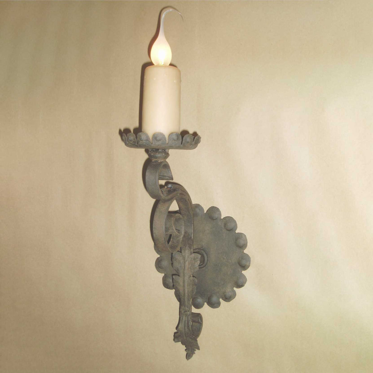 A decorative wall sconce featuring an elegant wrought iron design, with an intricately shaped candle holder and a softly glowing candle. The fixture showcases a charming, traditional aesthetic and ornate craftsmanship.