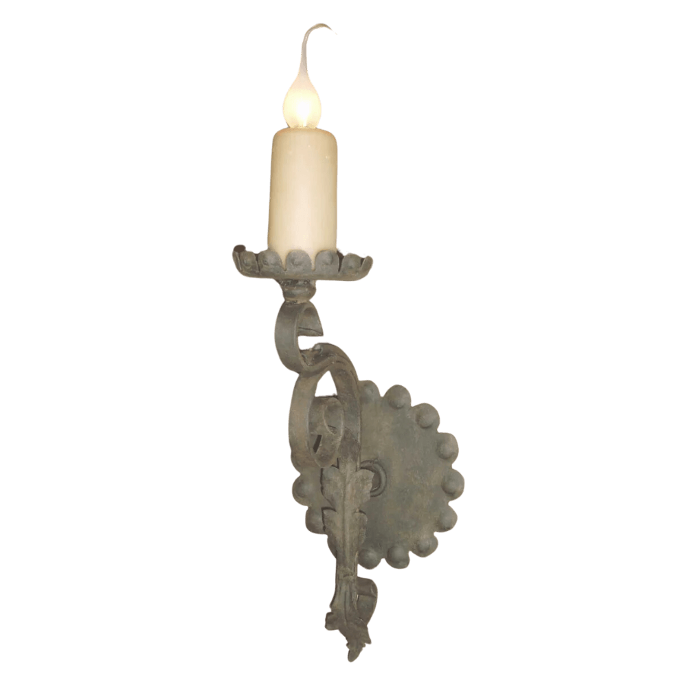 A rustic wrought iron wall sconce featuring a decorative base and a scalloped candle holder, topped with a softly glowing candle.