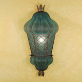 A decorative wall sconce featuring a unique shape with a glass shade in a rich teal hue, highlighted by intricate wrought iron detailing. The fixture has an elegant, vintage-inspired design, adding charm and character to any space.