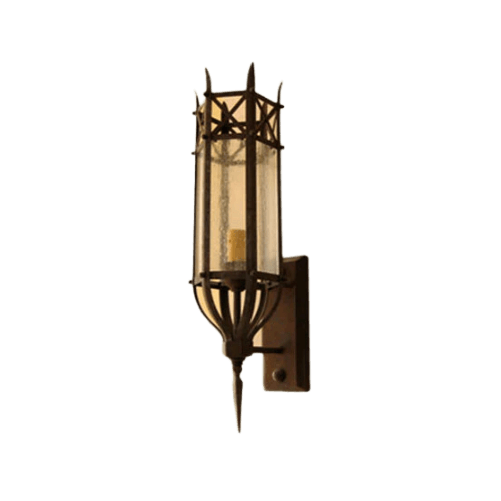 A sleek wrought iron wall sconce featuring a cylindrical glass shade with decorative ironwork. The design incorporates a pointed base and intricate detailing, creating an elegant illumination effect suitable for diverse interiors.