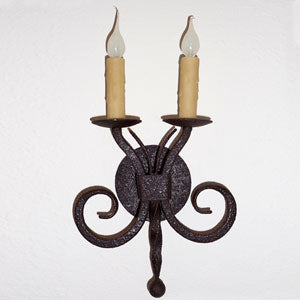 A beautifully crafted wrought iron sconce featuring two candle holders with light bulbs. The design includes elegant curves and a textured finish, adding a rustic charm suitable for various settings.