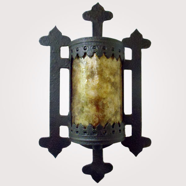 A decorative wall sconce featuring intricate wrought iron detailing and a cylindrical amber glass center. The design showcases elegant cutouts and ornate accents, creating a warm, inviting glow for any space.