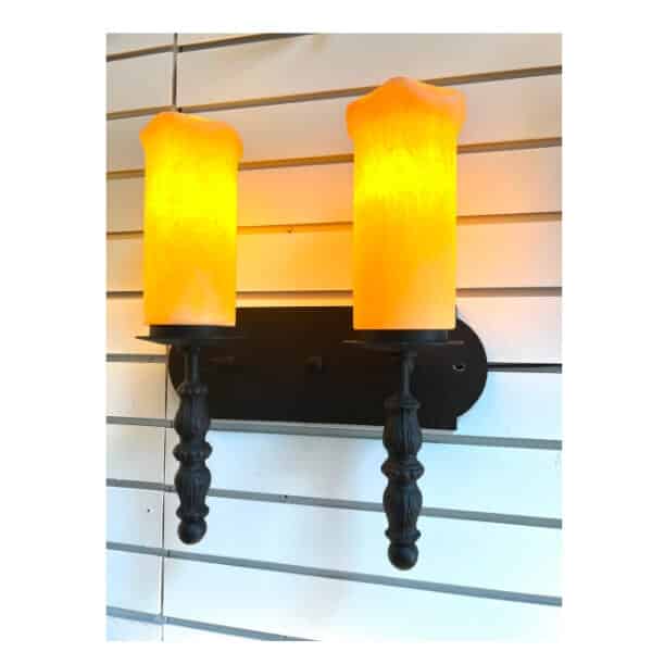 A wall-mounted sconce featuring two glowing candle-like fixtures with a warm yellow hue. The elegant design showcases intricate black wrought iron detailing, enhancing the ambiance of any room with its rustic charm.