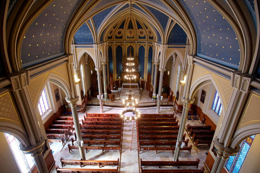 An ornate cathedral interior showcasing vaulted ceilings adorned with a starry blue pattern, elegant columns, wooden pews, and a grand chandelier illuminating the central altar.