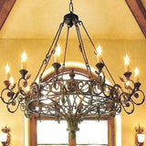 A beautifully crafted wrought iron chandelier featuring intricate scrollwork and elegant candle holders. The warm glow from the candles illuminates the piece, enhancing its classic charm against a soft-colored wall.