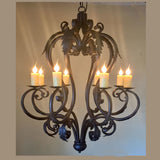 A beautifully crafted wrought iron chandelier featuring intricate scrollwork and leaf designs. Six candle holders with flickering flames add a warm, inviting glow, perfect for enhancing any space's ambiance.